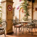 Terrasse de café espagnole ensoleillée avec panneau d'interdiction de fumer, illustrant le projet de loi espagnol sur l'extension des zones sans tabac et sans vape